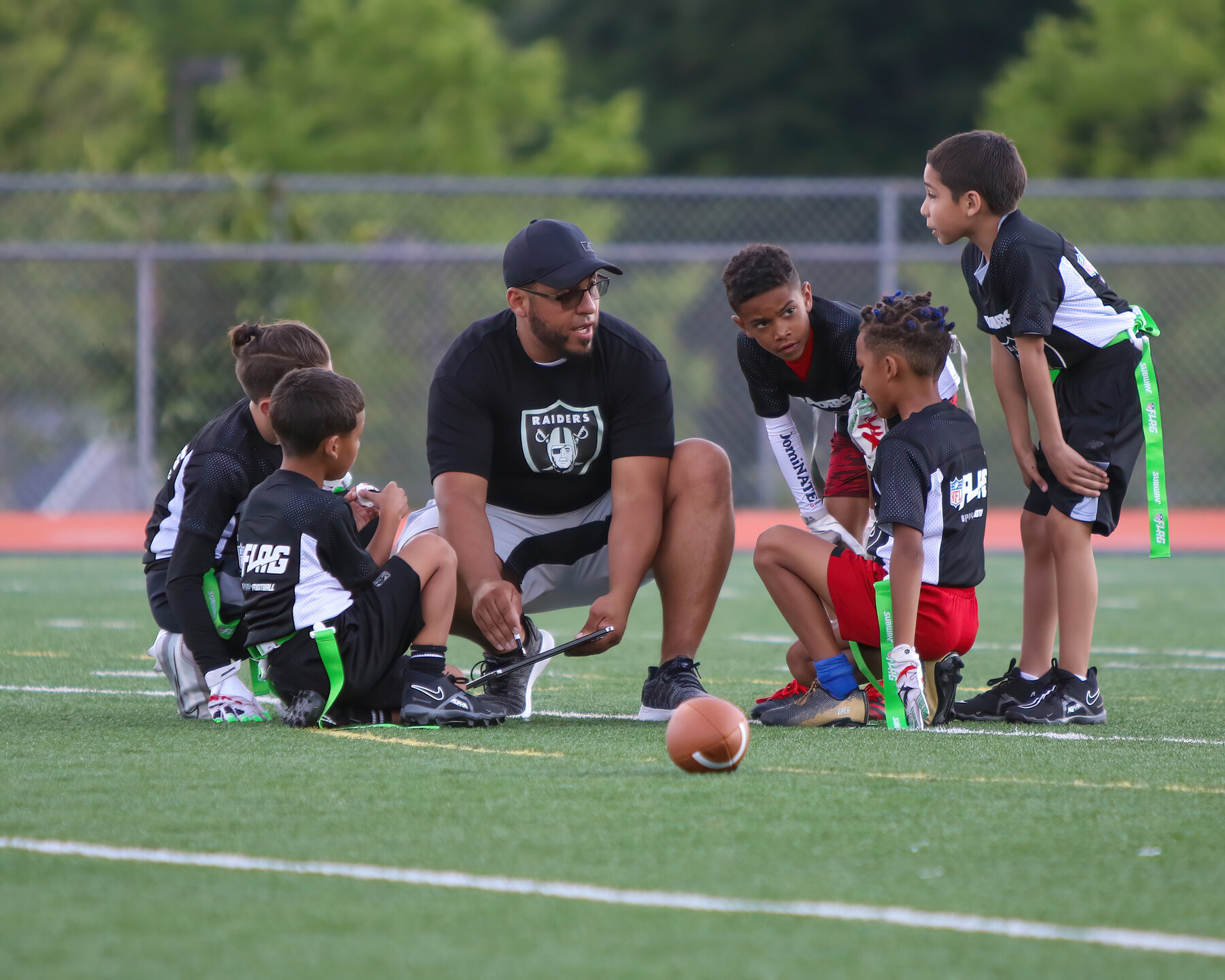 A coach kneeling with young flag football players to review a play